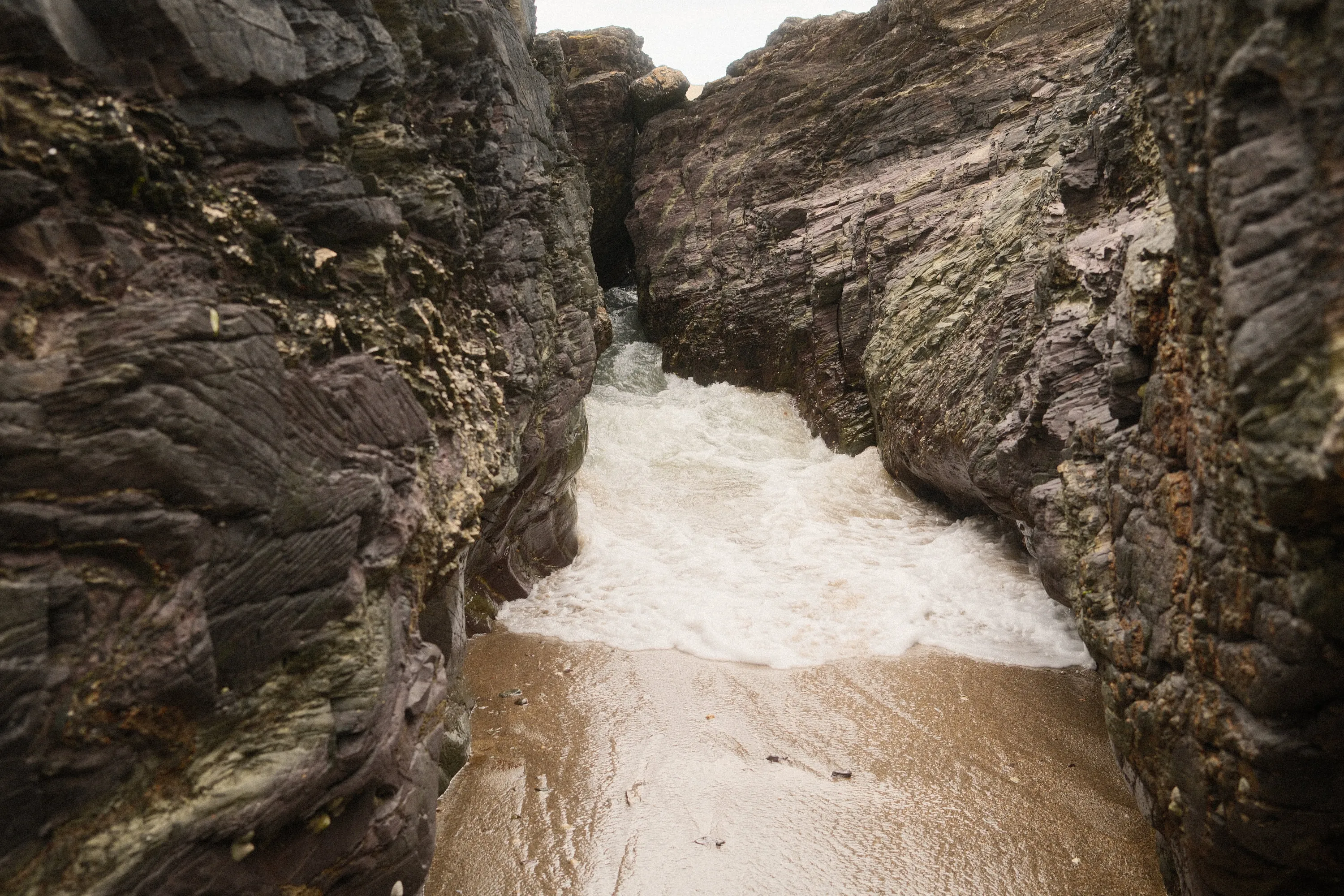 Surf running up a gully cut between the rocks.