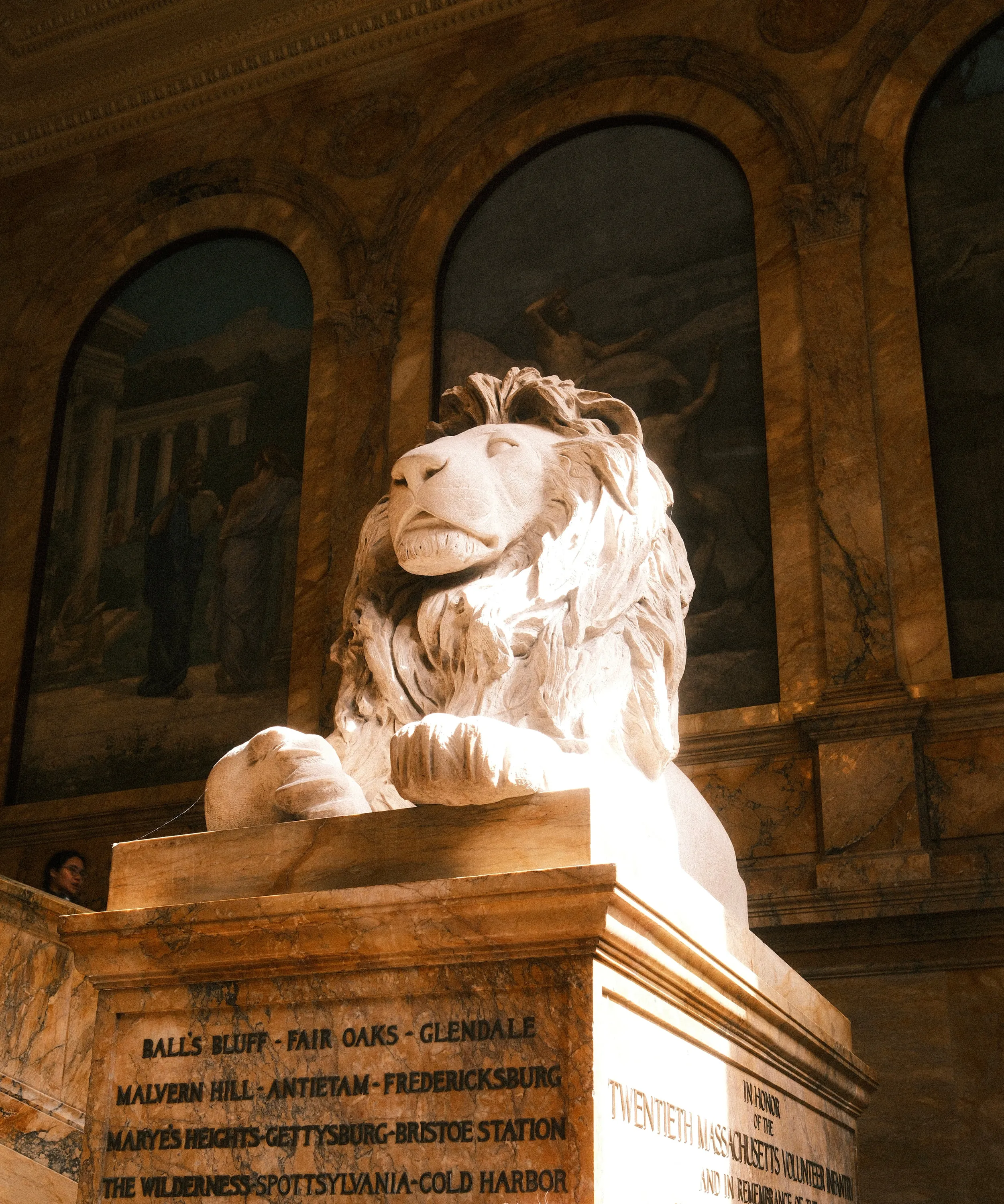 A marble lion on the library stairs, battle names cut into the plinth.